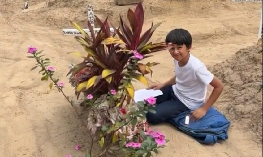 Niño hace la tarea junto a la tumba de su madre